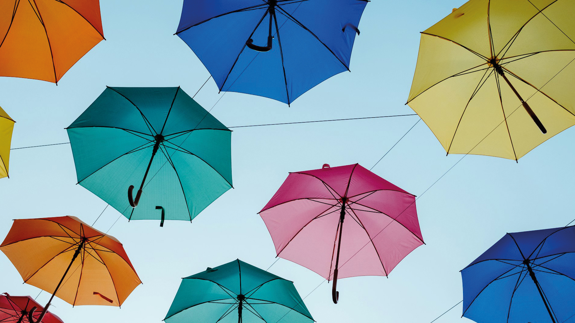 Das Bild stellt verschiedenfarbige Regenschirme dar, die netzartig im Himmel hängen. Das Bild wird als Visual zu einem Blogartikel der Website von Beckerkommunikation verwendet, um den Artikel Freelance Art Direction für Ihr Unternehmen zu verdeutlichen.